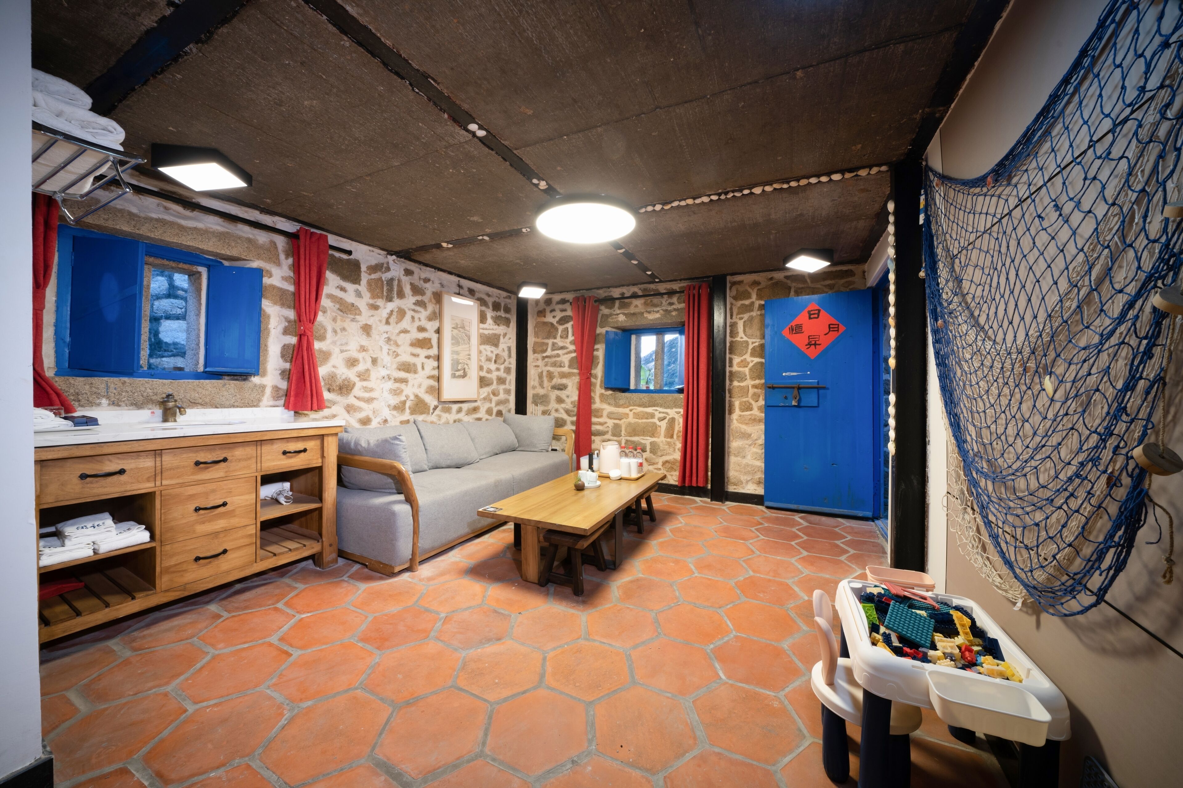 A room with a stone wall, a wooden table, a sofa, and a small play area with toys.