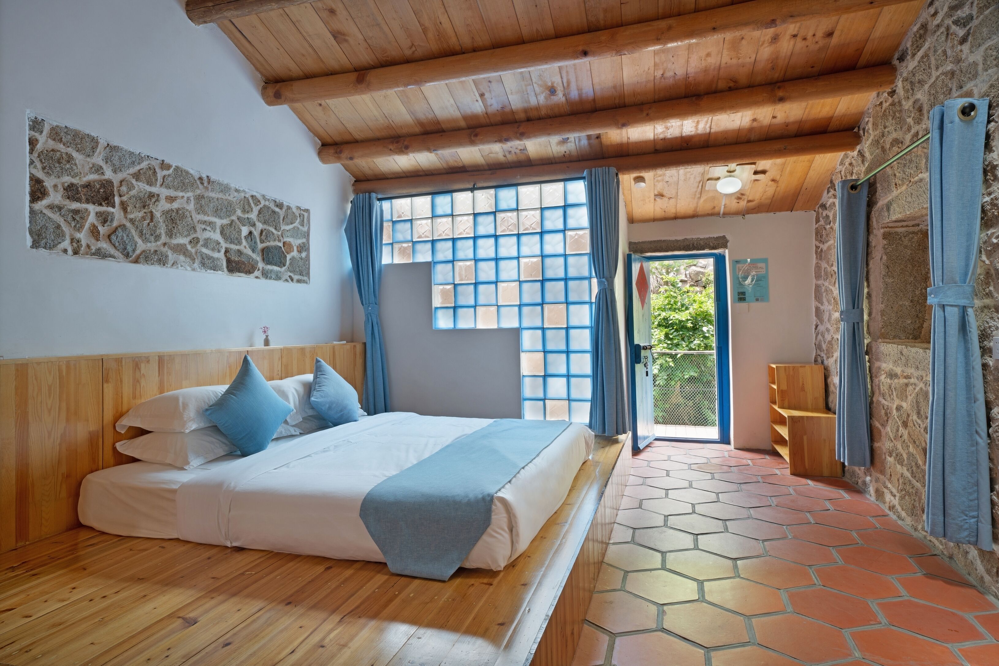 A bedroom with a wooden bed, stone wall, and a view of the outside.