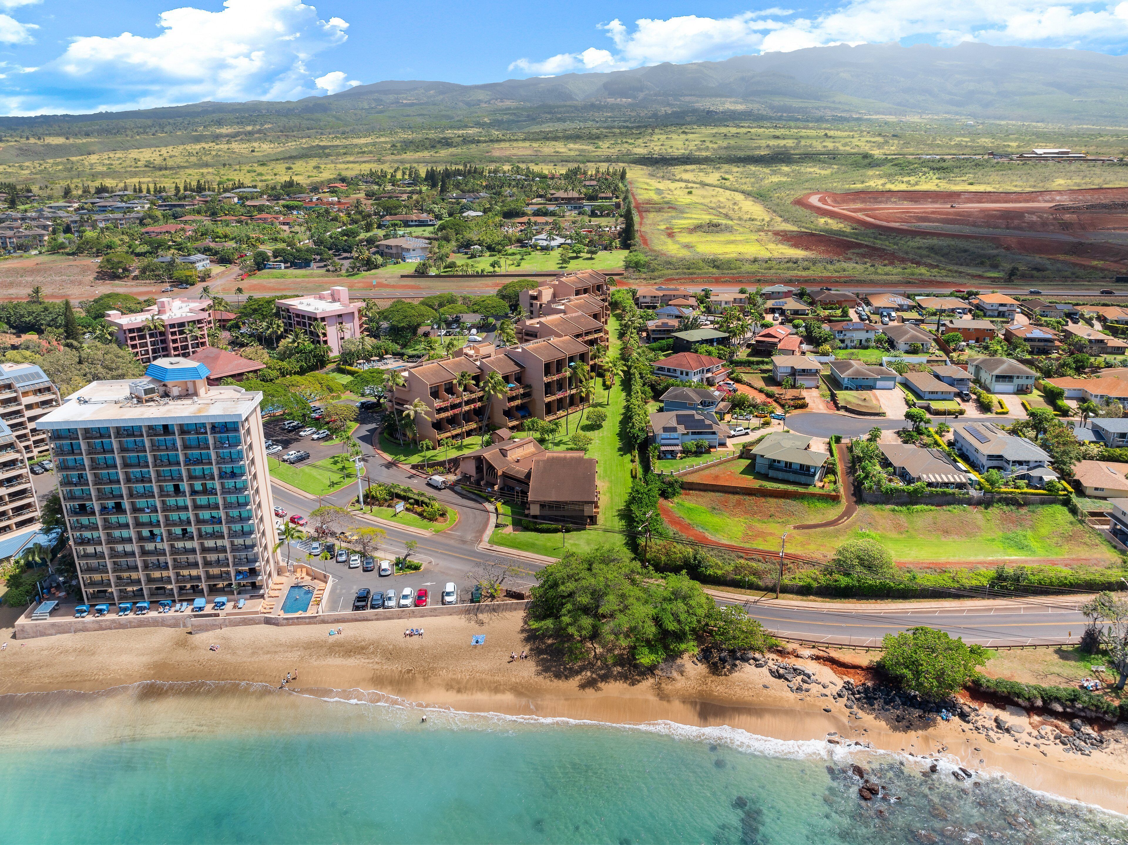 Un quartier résidentiel situé sur la côte, avec une plage, des maisons et un grand bâtiment doté d’une piscine.