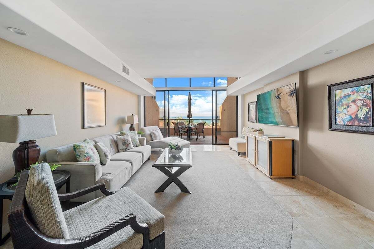 Amplia sala de estar con un gran ventanal con vista al mar, un conjunto de sofás cómodos, una mesa de centro y un televisor en la pared.