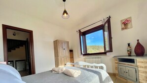 Un dormitorio con cama, armario, radiador, ventana con vistas y lámpara colgante.