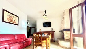 Una sala de estar con un sofá de cuero rojo, una mesa de comedor de madera, sillas, un televisor y una chimenea.