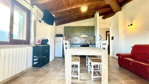 A spacious living area with a wooden ceiling, a dining table with white chairs, a red sofa, and a kitchen with green cabinets. - Maion Bellevue con Patio (Cardedu)