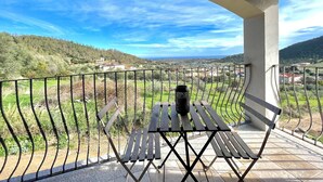 A balcony with a table and chair, overlooking a scenic landscape with hills and a distant view of the sea. - Maion Bellevue con Patio (Cardedu)