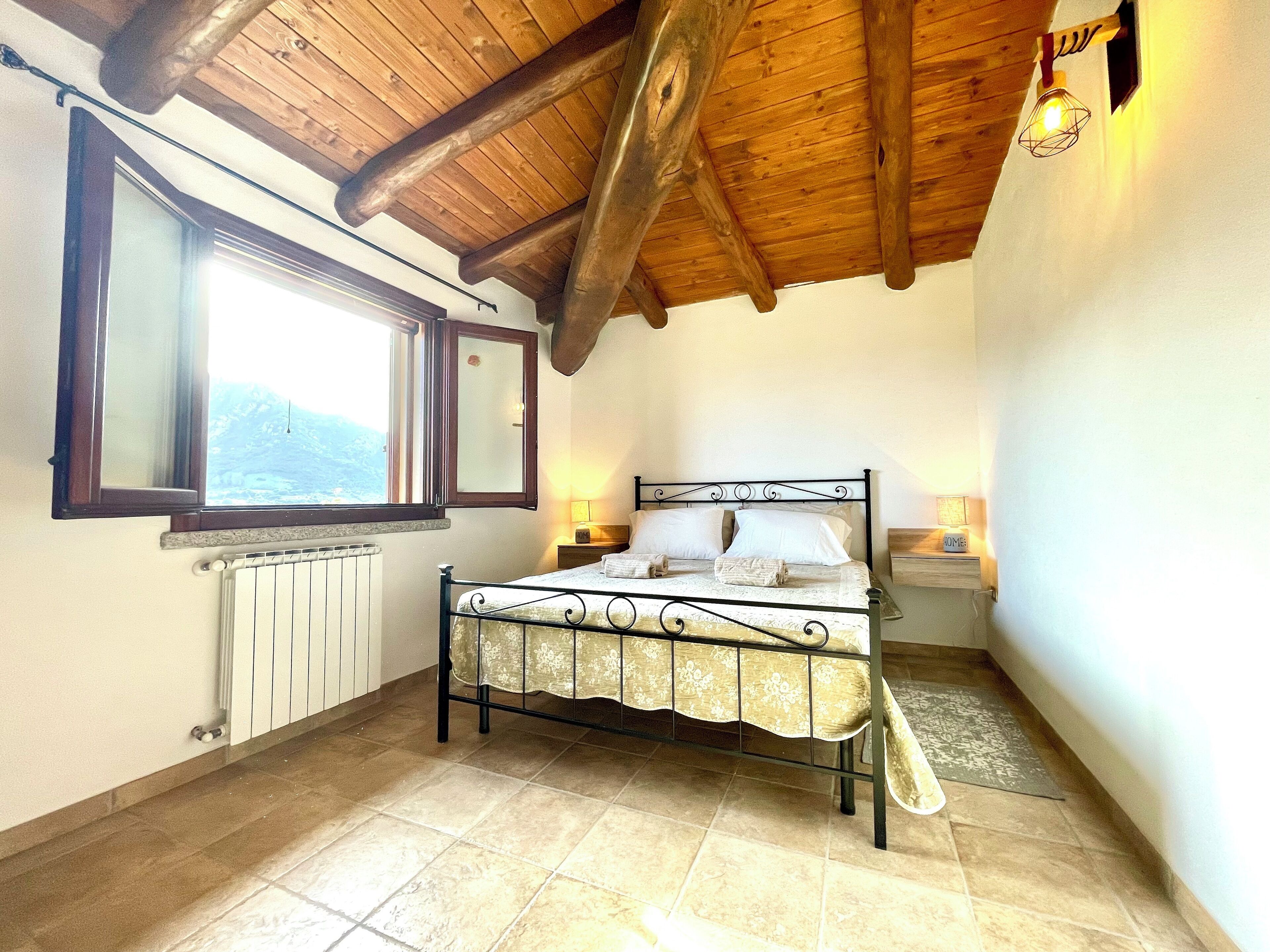 A bedroom with a wooden ceiling, a bed with a metal frame, a window, and a radiator.