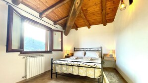 A bedroom with a wooden ceiling, a bed with a metal frame, a window, and a radiator. - Maion Bellevue con Patio (Cardedu)