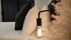 A neatly made bed with a white quilt, a black pillow, and a decorative light fixture.