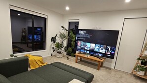 A modern living room with a large flat-screen TV, a green sofa, a brown bean bag, and a small wooden table.