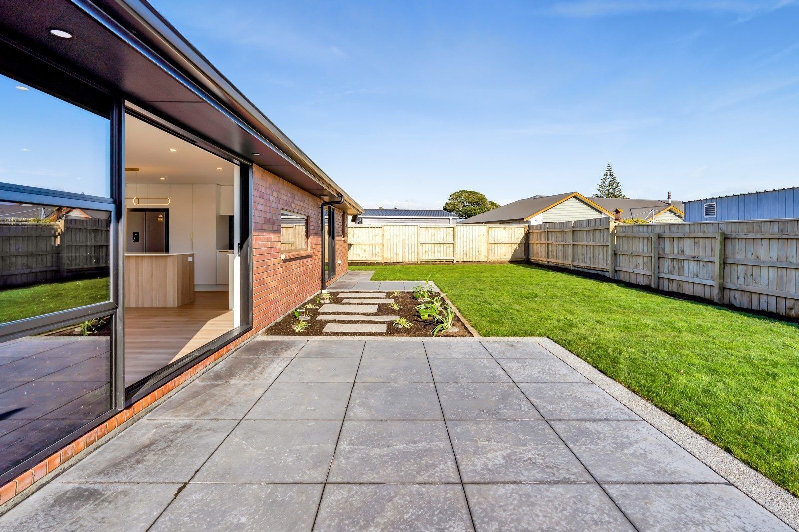 A modern house with a patio, a brick exterior, and a view of the backyard.