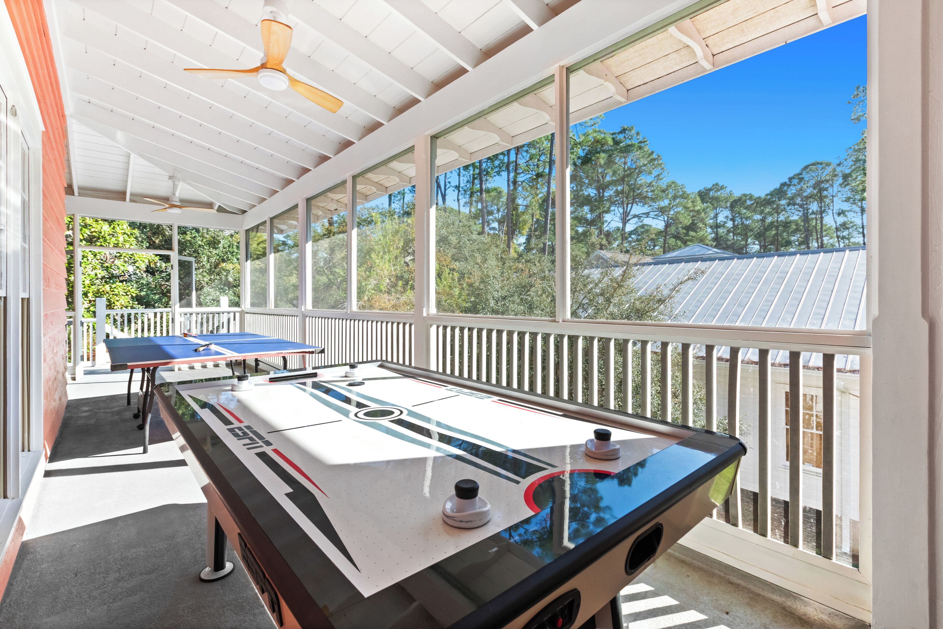 An indoor table tennis table with a view of trees and a house through large windows.