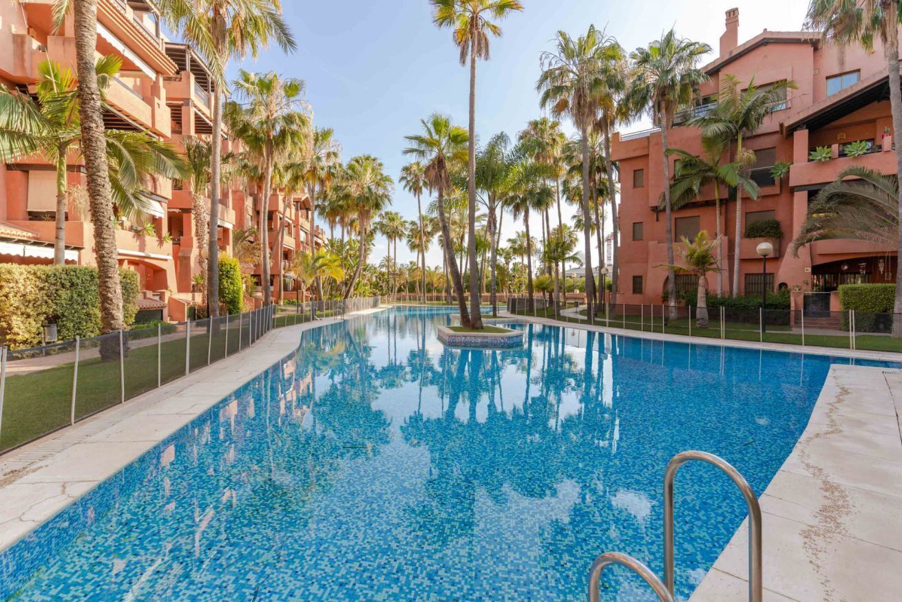 A swimming pool surrounded by palm trees and multi-story buildings.