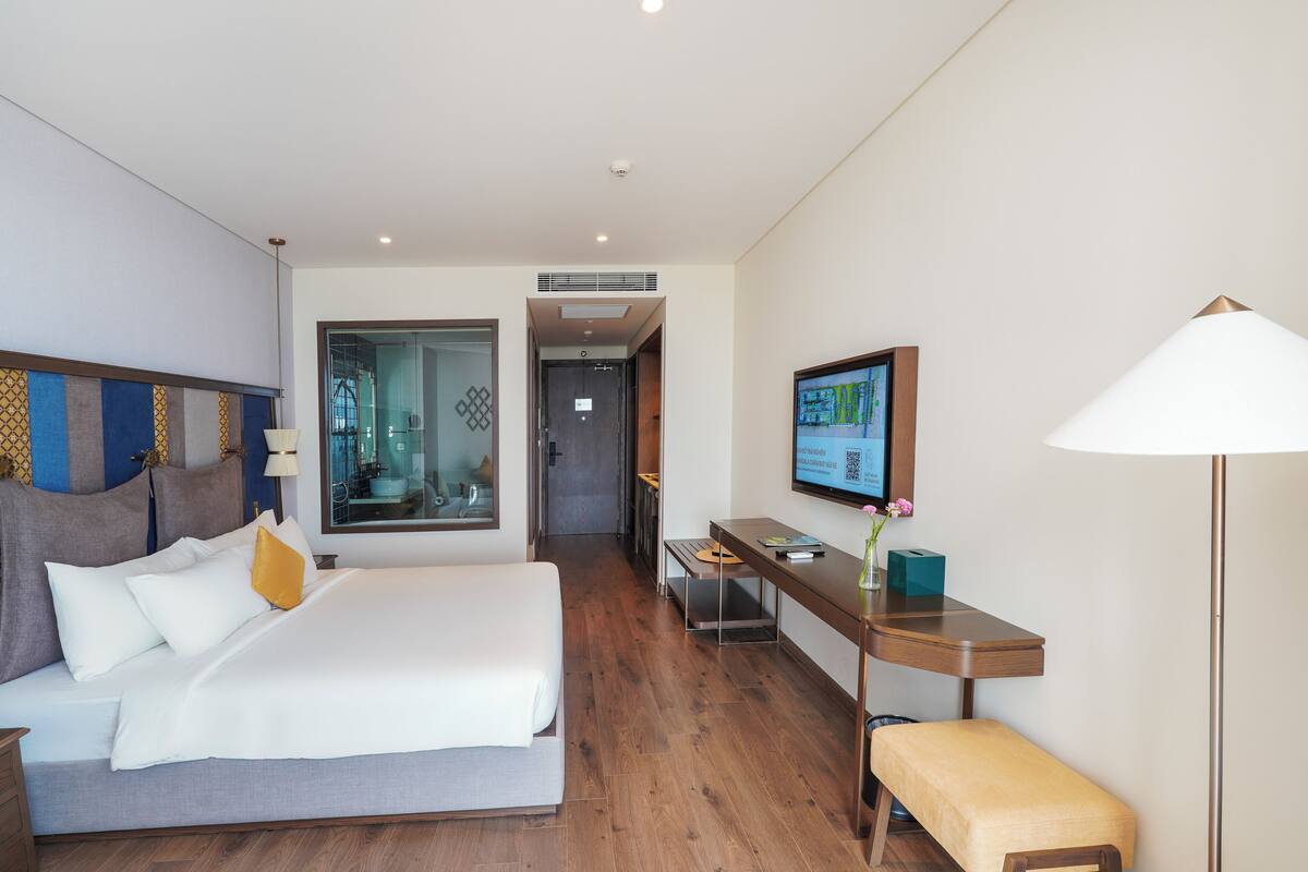 A hotel room with a bed, bedside table, desk, chair, and a television.