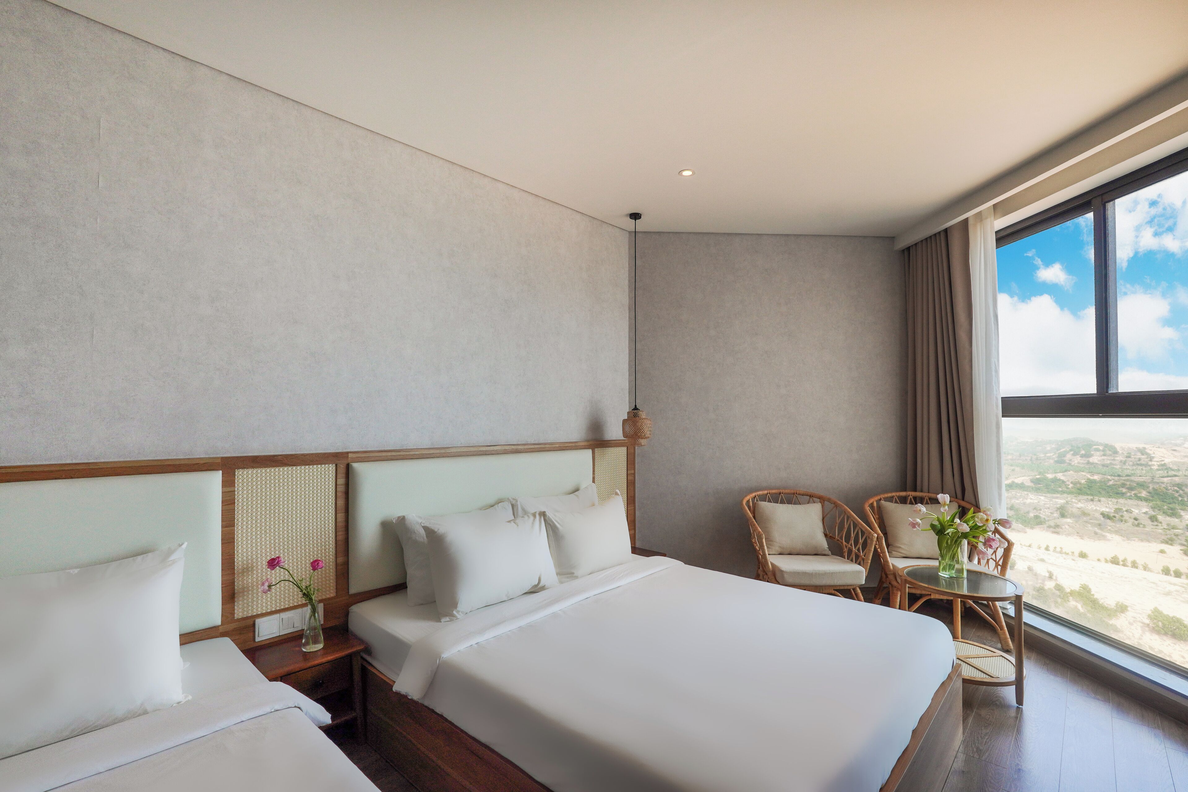 Een hotelkamer met twee bedden, een zithoek met stoelen, een kleine tafel en uitzicht op het landschap.