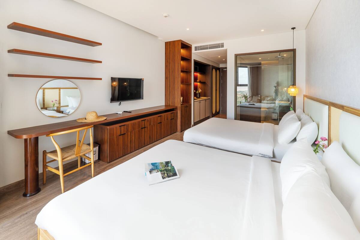 A modern hotel room with a bed, a desk, a TV, and a bathroom visible through a glass door.