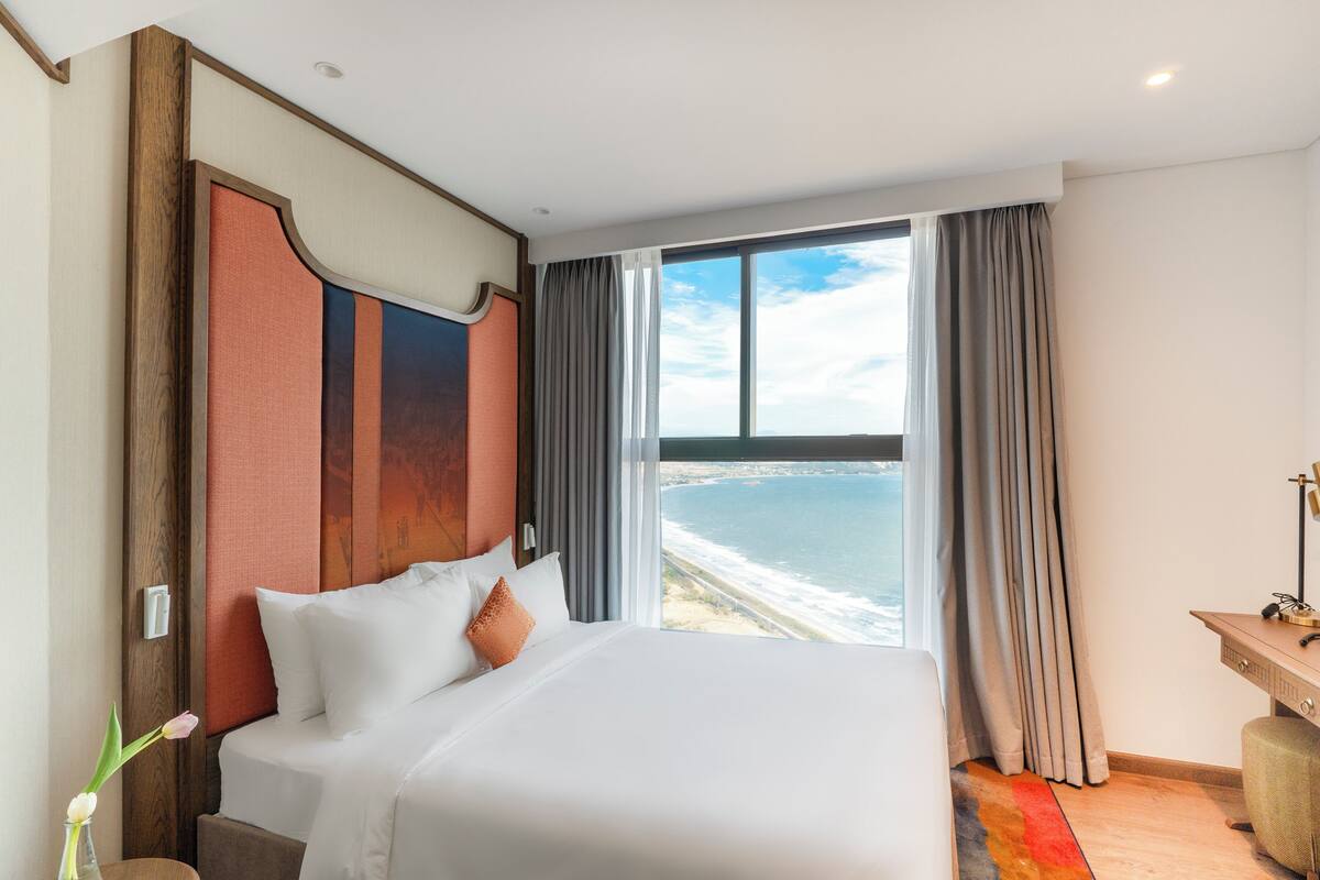 A hotel room with a large bed, a desk, and a view of the ocean.