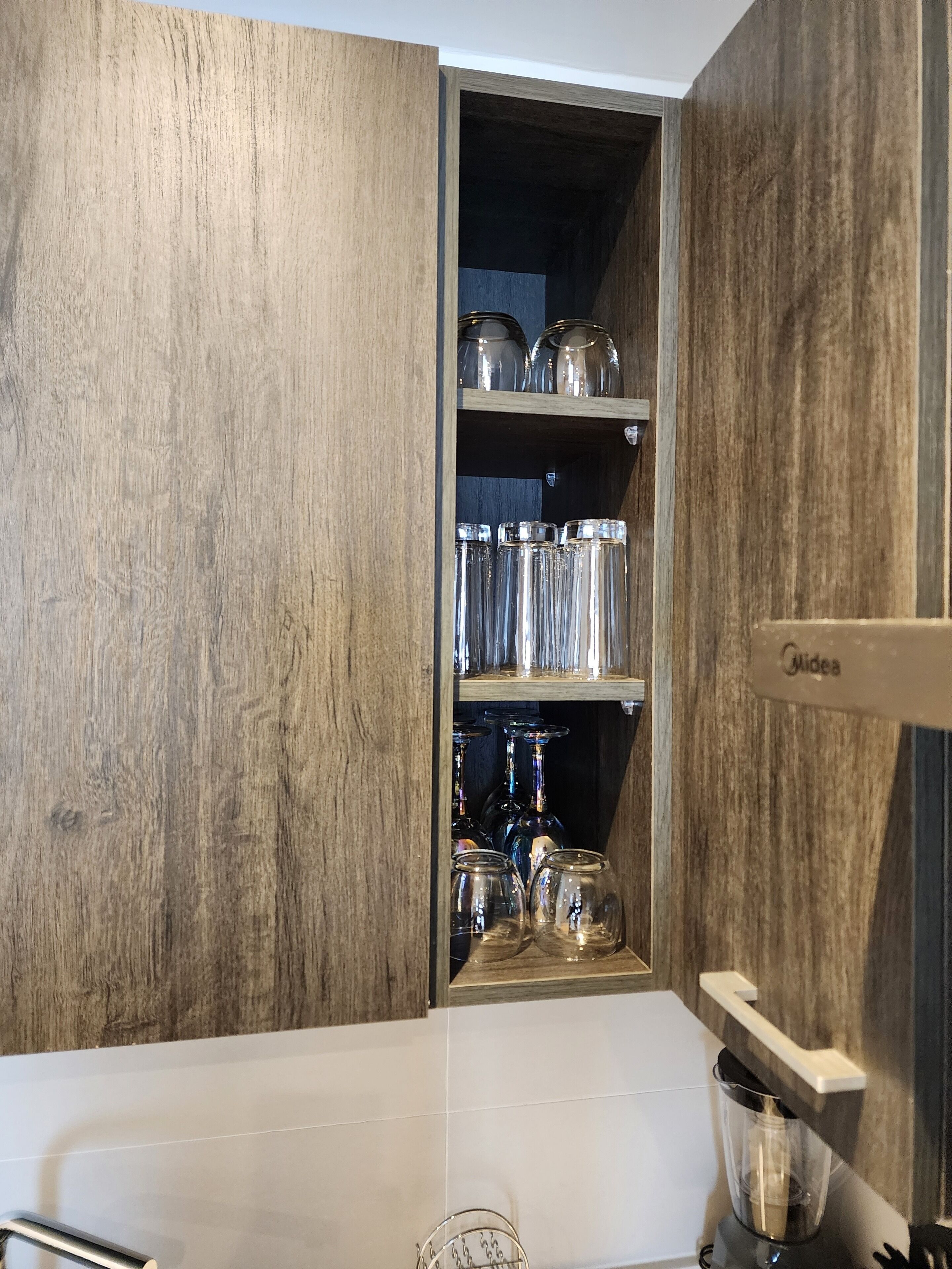 Une cuisine avec des meubles en bois, un plan de travail blanc et un meuble-bar intégré contenant différents types de verres.