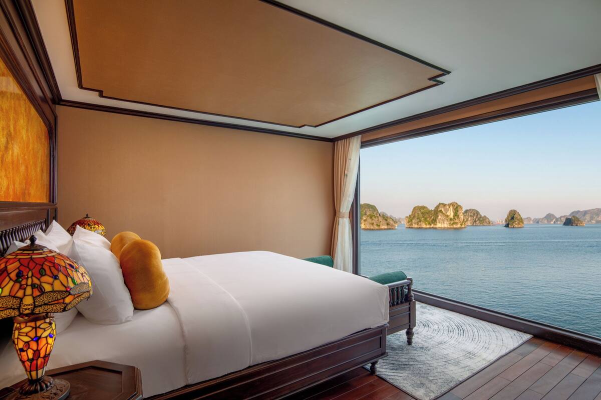 Quarto com cama grande, mesa de cabeceira, luminária e vista para a água e ilhas.