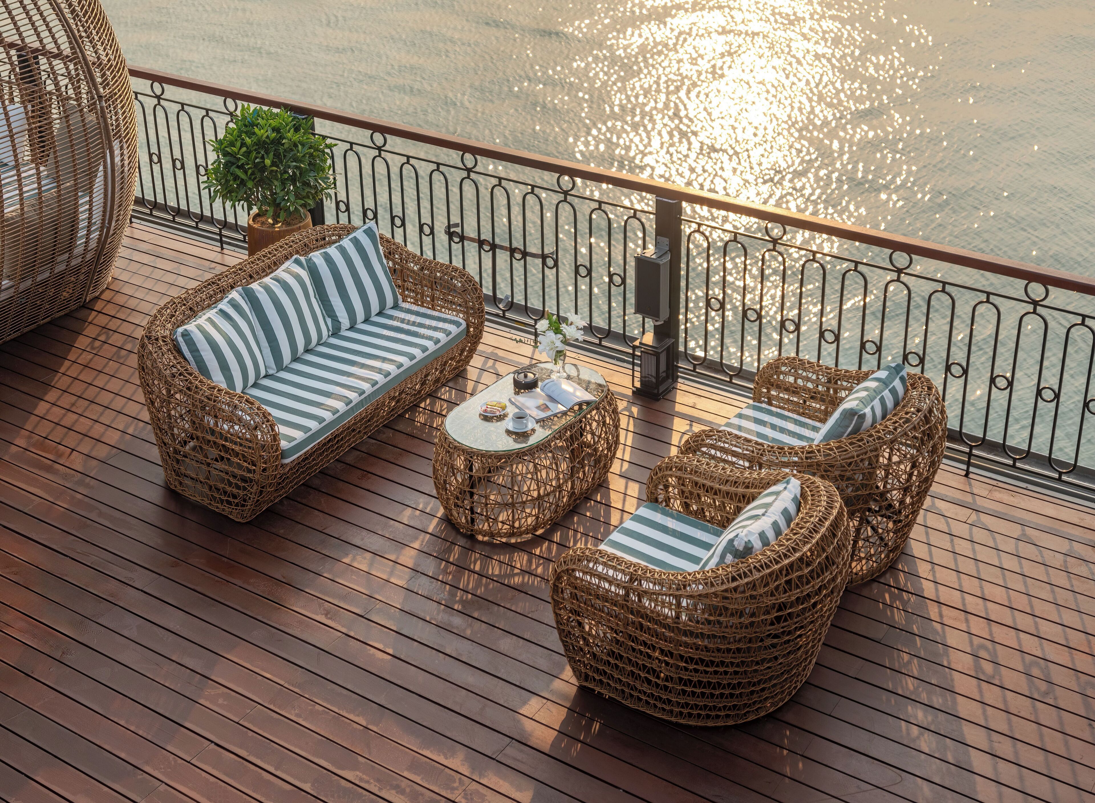 A deck with wicker furniture, including a sofa and armchairs, a glass coffee table, and a potted plant.