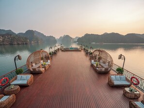 A wooden deck with wicker furniture and a view of the water. - Indochine Grand Lan Ha Bay (Tuan Chau)