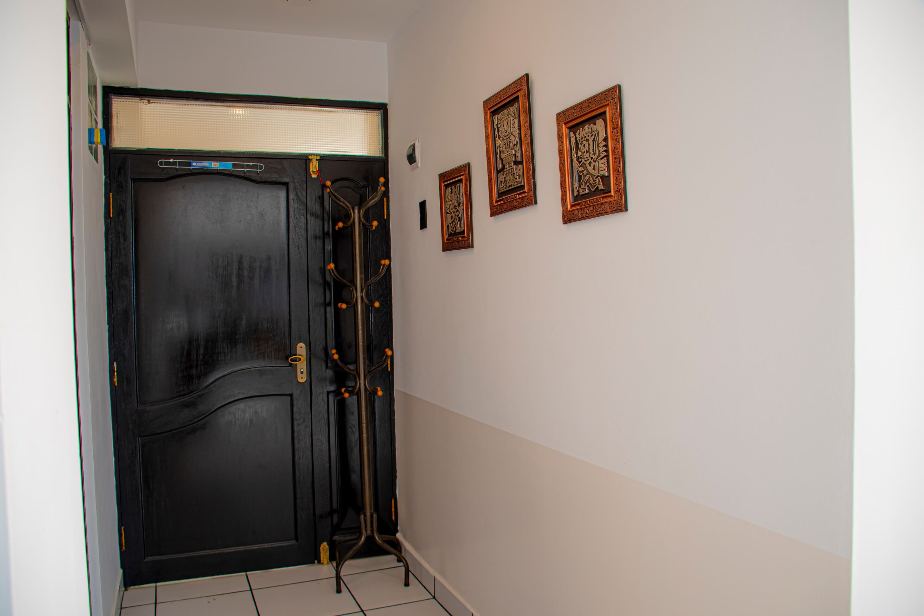 A black door with a brass handle and a coat rack with hooks. There are three framed pictures on the wall.