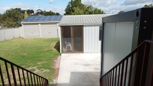 A backyard with a concrete patio, a fenced area, and a building with solar panels. - Cozy sleep out  with free wi-fi (Kennington)