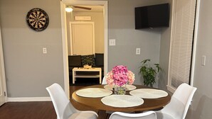 A dining area with a round table, white chairs, a ceiling fan, a dartboard, and a TV mounted on the wall. - Peaceful Arlington Home (Arlington)