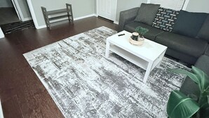 A living room with a white coffee table, a gray sofa, a patterned rug, a clock, and a door. - Peaceful Arlington Home (Arlington)