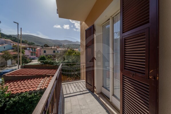 A balcony with a tiled floor, a metal railing, and a view of a residential area with houses and hills in the background.