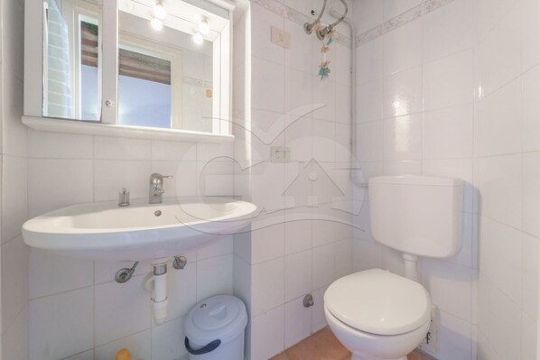 A bathroom with a white sink, toilet, and a trash bin.