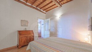 Un dormitorio con cabecera de madera, cama con colcha a rayas, cómoda de madera y una puerta que da a otra habitación.