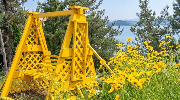 A yellow swing set in a natural setting with a lake and trees in the background. - Yeosu Island Pet Pension (Yeosu)