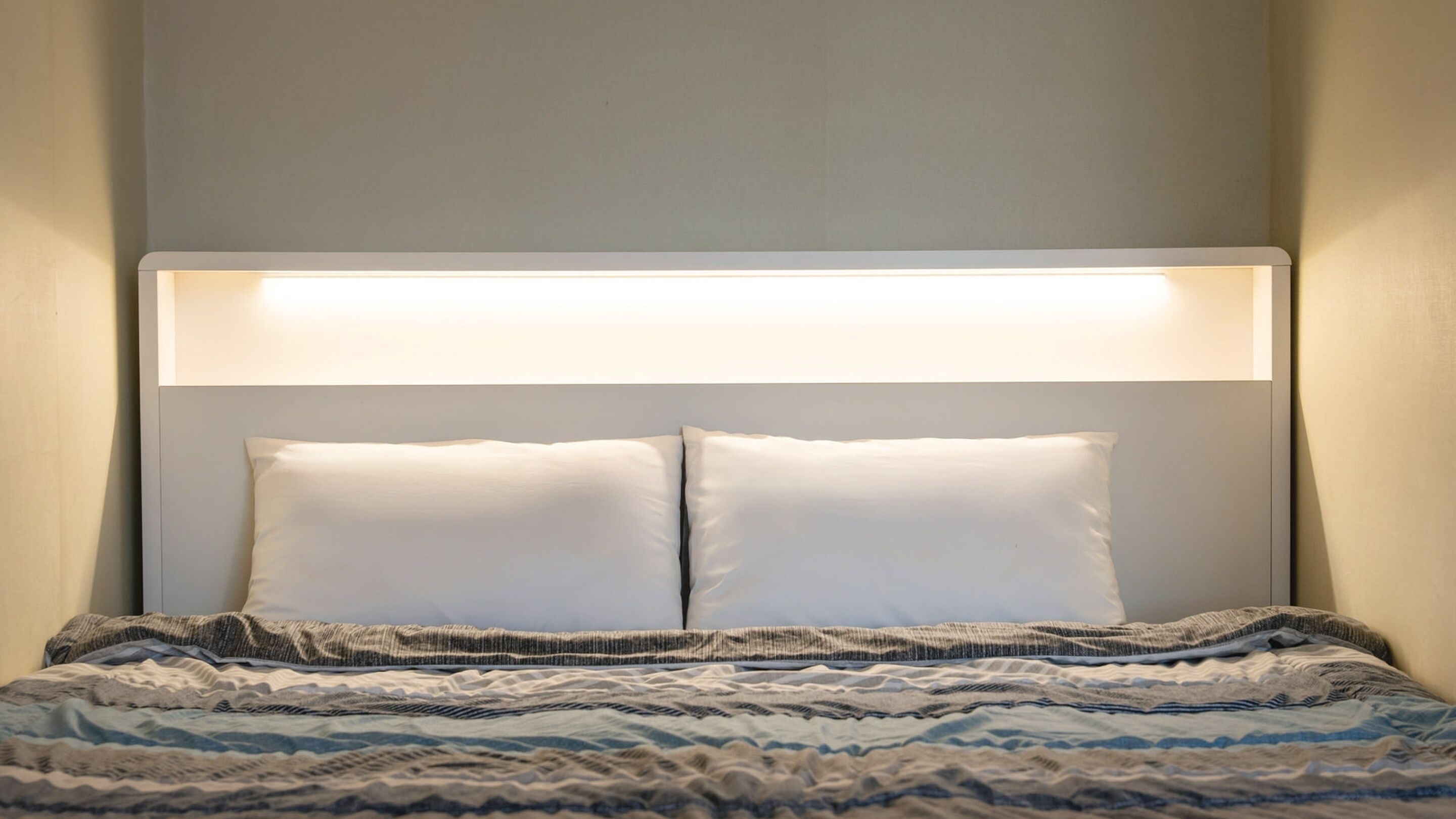 Una cama con cabecera, dos almohadas y una manta estampada.