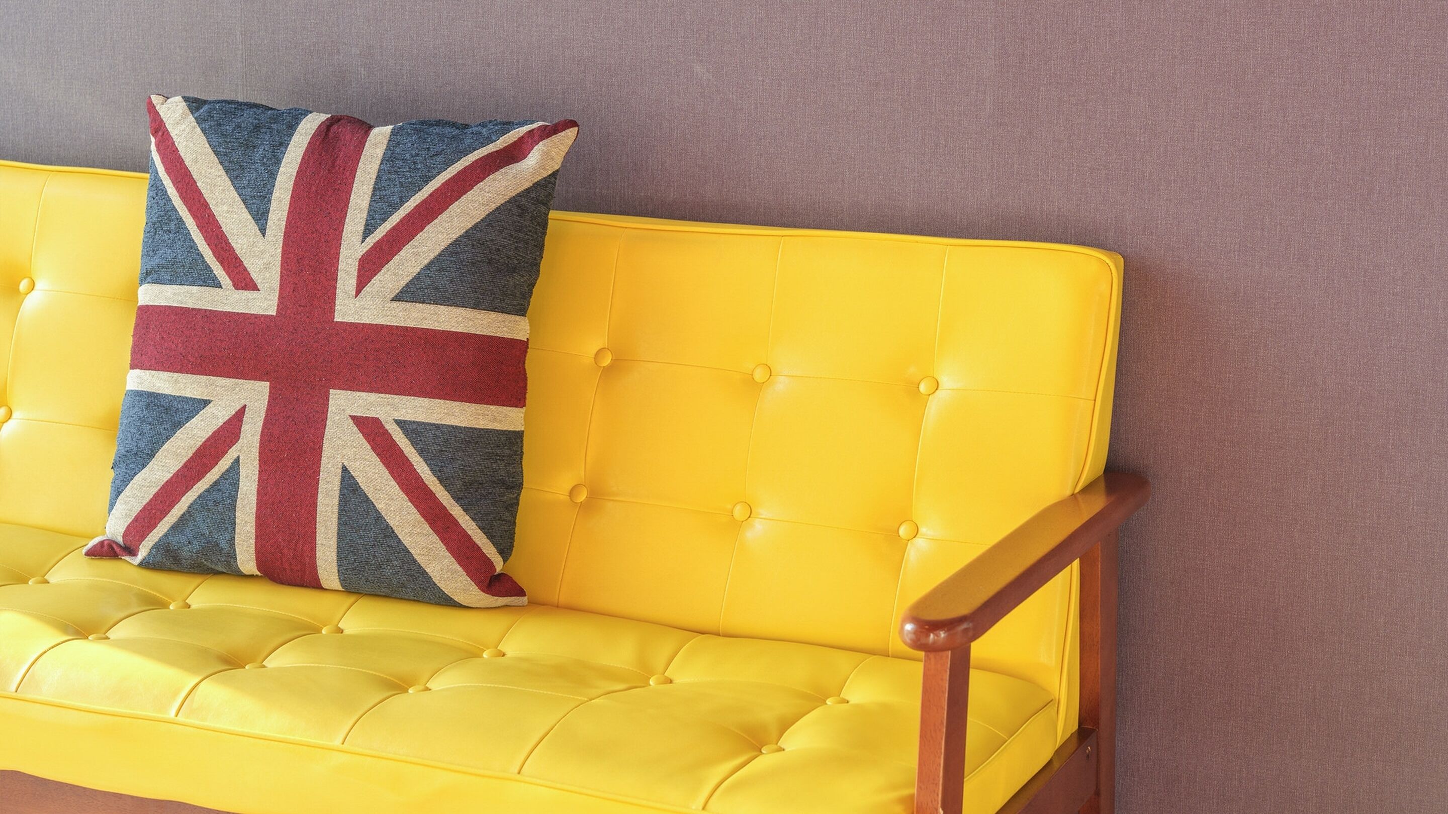 A yellow tufted sofa with a Union Jack pillow against a purple wall.