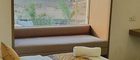 A hotel room with a bed, a window with a view of the outdoors, and an air conditioning unit above the window.
