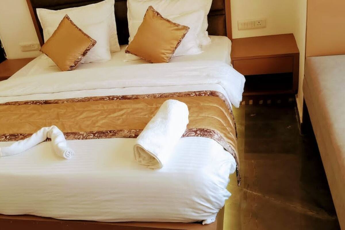 A neatly made bed with white and brown bedding, a rolled towel, and a wooden nightstand beside it.