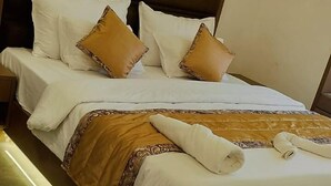 Una cama bien tendida con ropa de cama blanca y marrón, un cabecero de madera y una almohada pequeña blanca al lado.