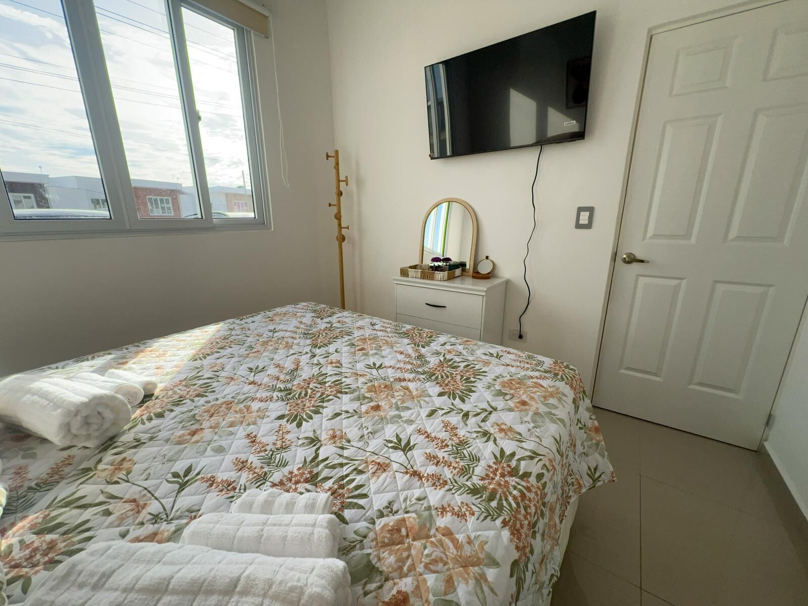 Ein Schlafzimmer mit einem Bett, einem an der Wand montierten Fernseher, einem Schminktisch und einer Tür.