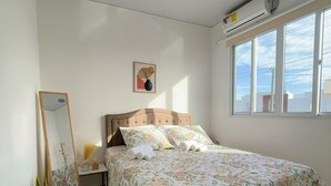 A bedroom with a bed, a bedside table, a mirror, and a window.