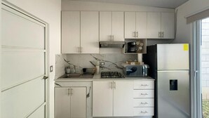 A modern kitchen with white cabinets, a built-in stove, a microwave, and a refrigerator.