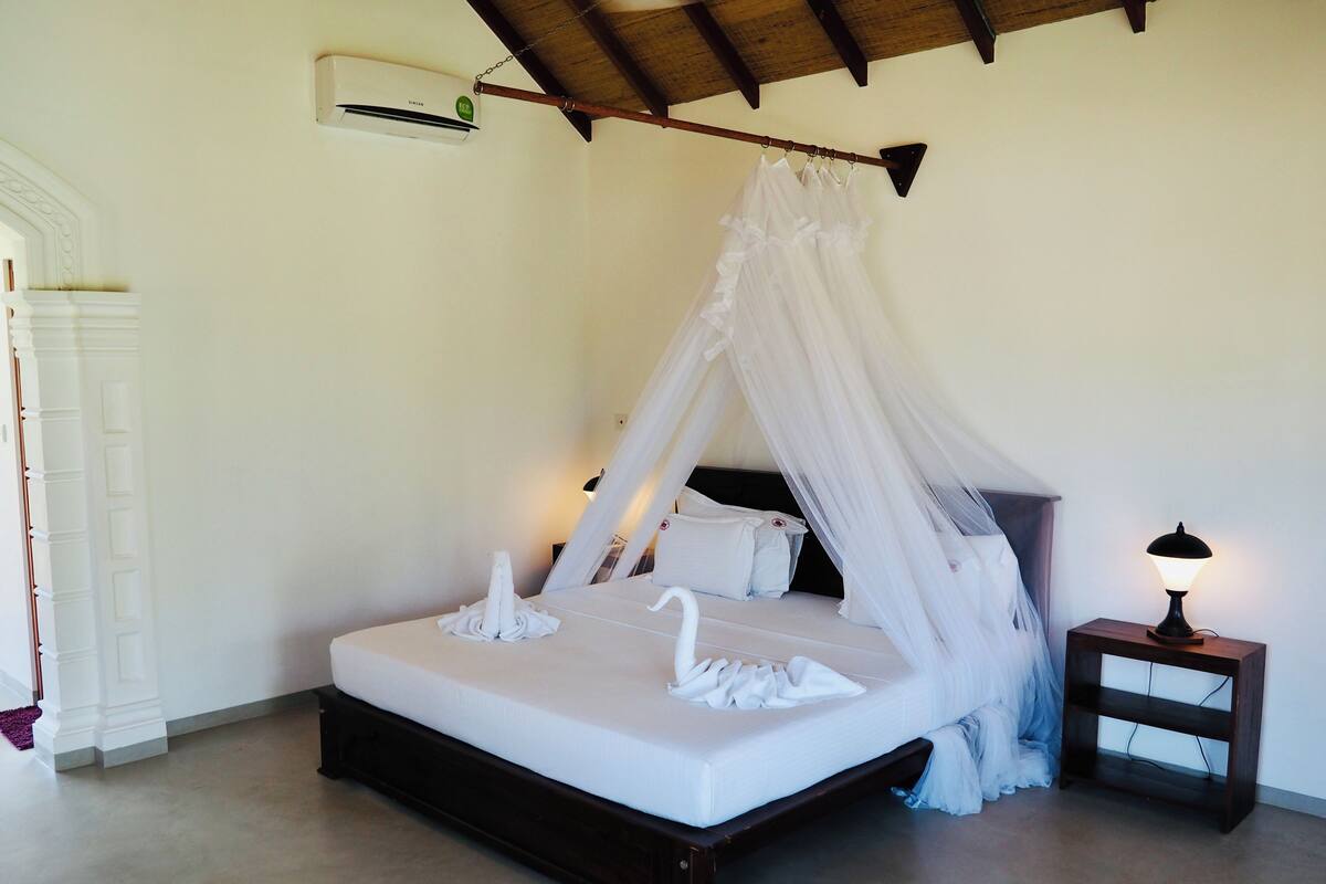 Un dormitorio con una cama con dosel, una mesita de noche con lámpara y un aire acondicionado de pared.