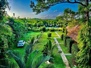 A lush garden with a swimming pool, a white car, and a thatched-roof structure. - Happy Man Village (Kosgoda)