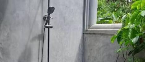 A concrete shower enclosure with a stone floor, a handheld showerhead, and a wall-mounted faucet.