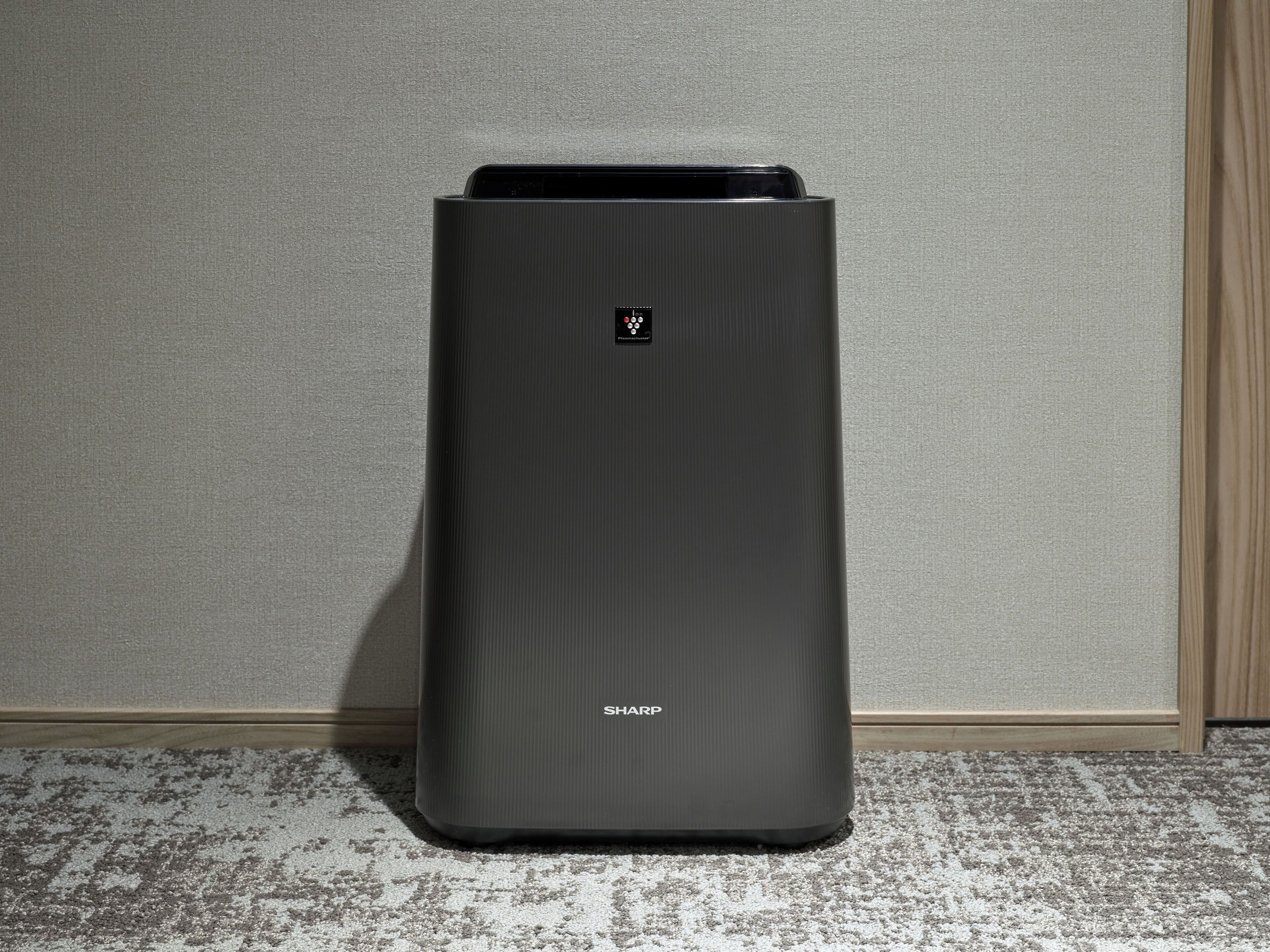 A black, rectangular, metallic object with a logo and the word "SHARP" on its side, standing on a textured floor against a plain wall.