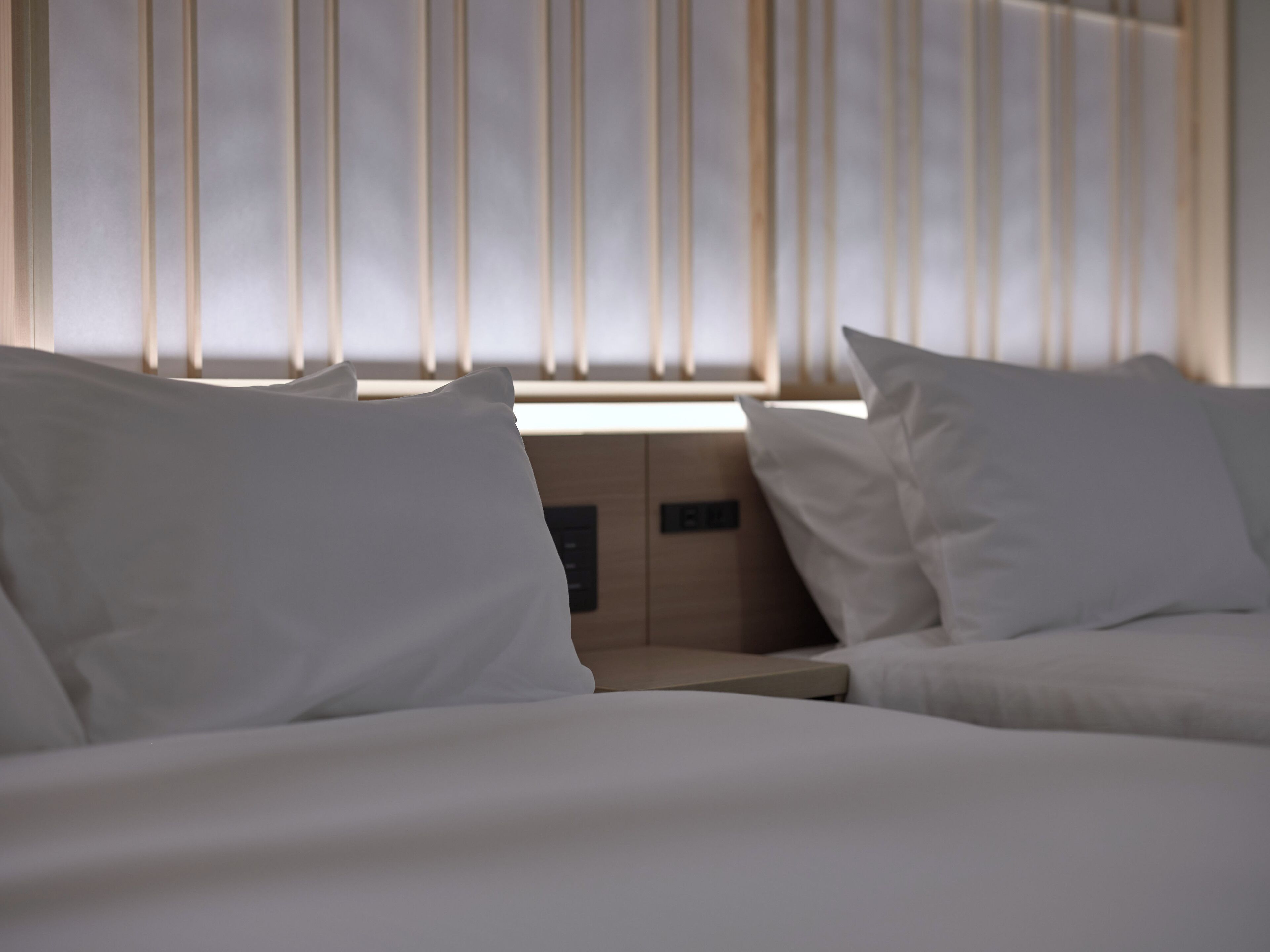 A hotel room with a bed, a nightstand, and a window with vertical blinds.