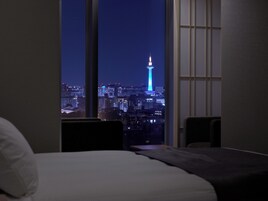 A hotel room with a large window offering a nighttime view of a cityscape, including a prominent tower.