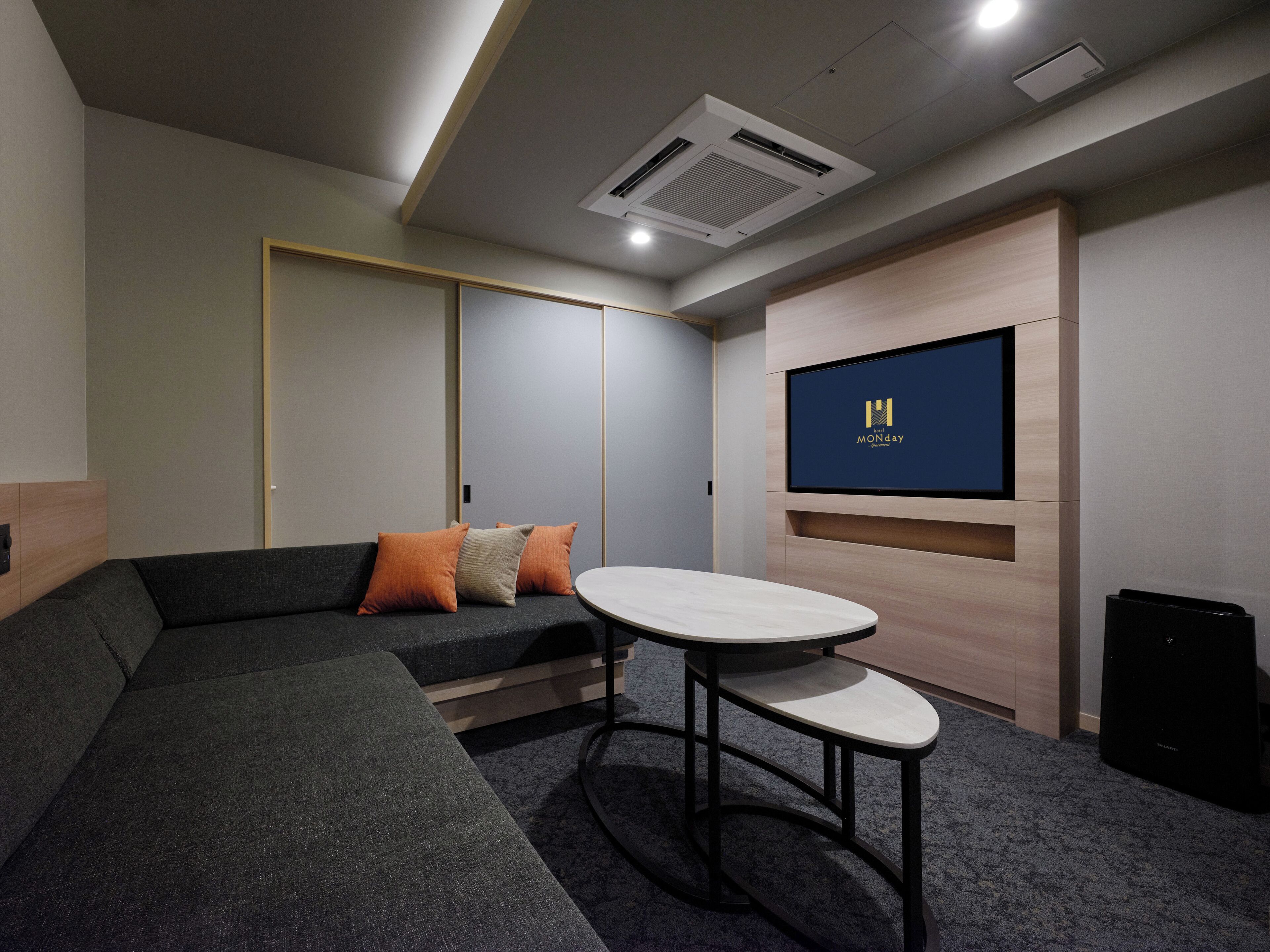 A modern conference room with a sectional sofa, a round table, a flat-screen TV, and a projector.