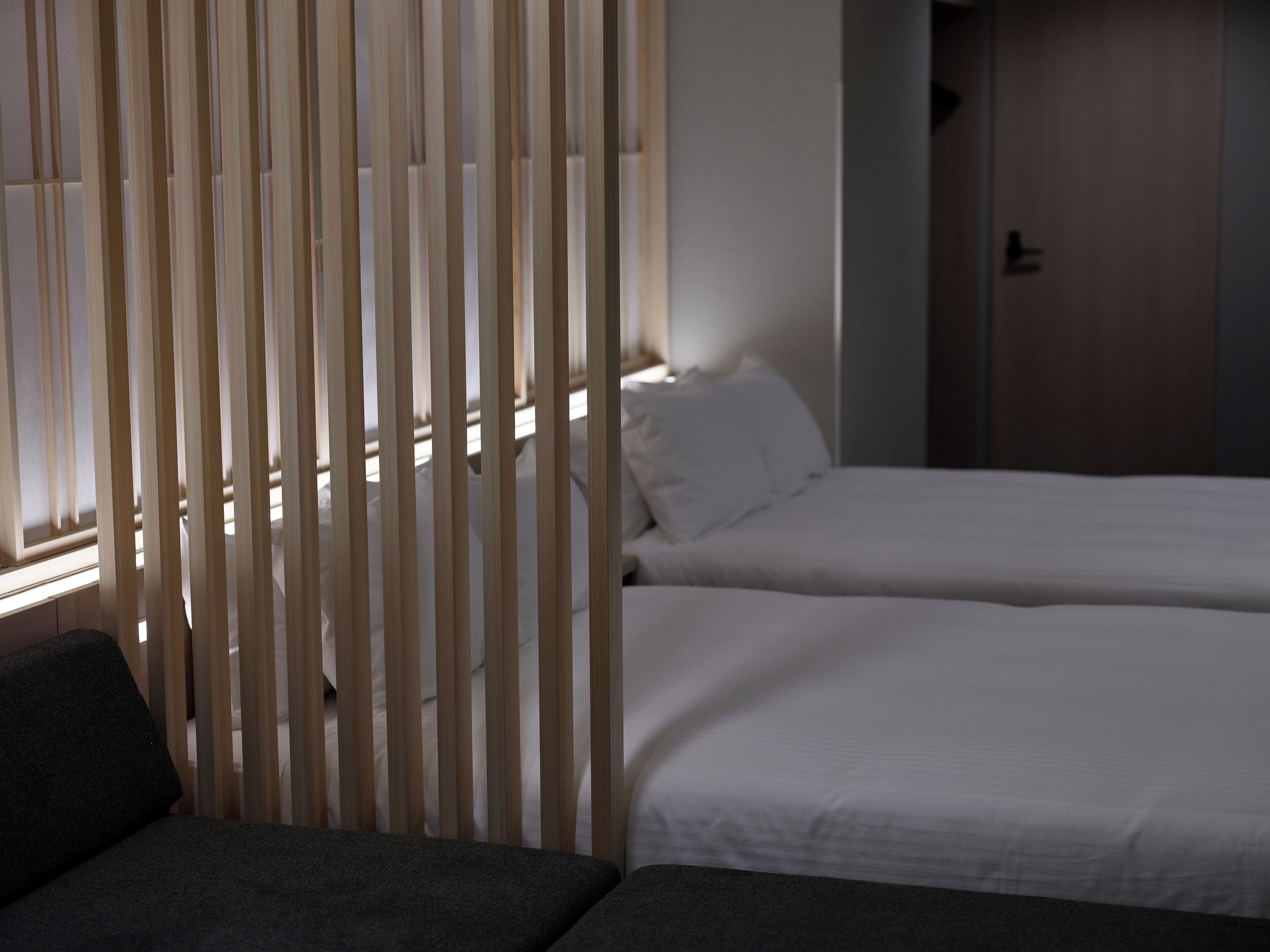 A hotel room with two beds, a wooden partition, and a sofa.