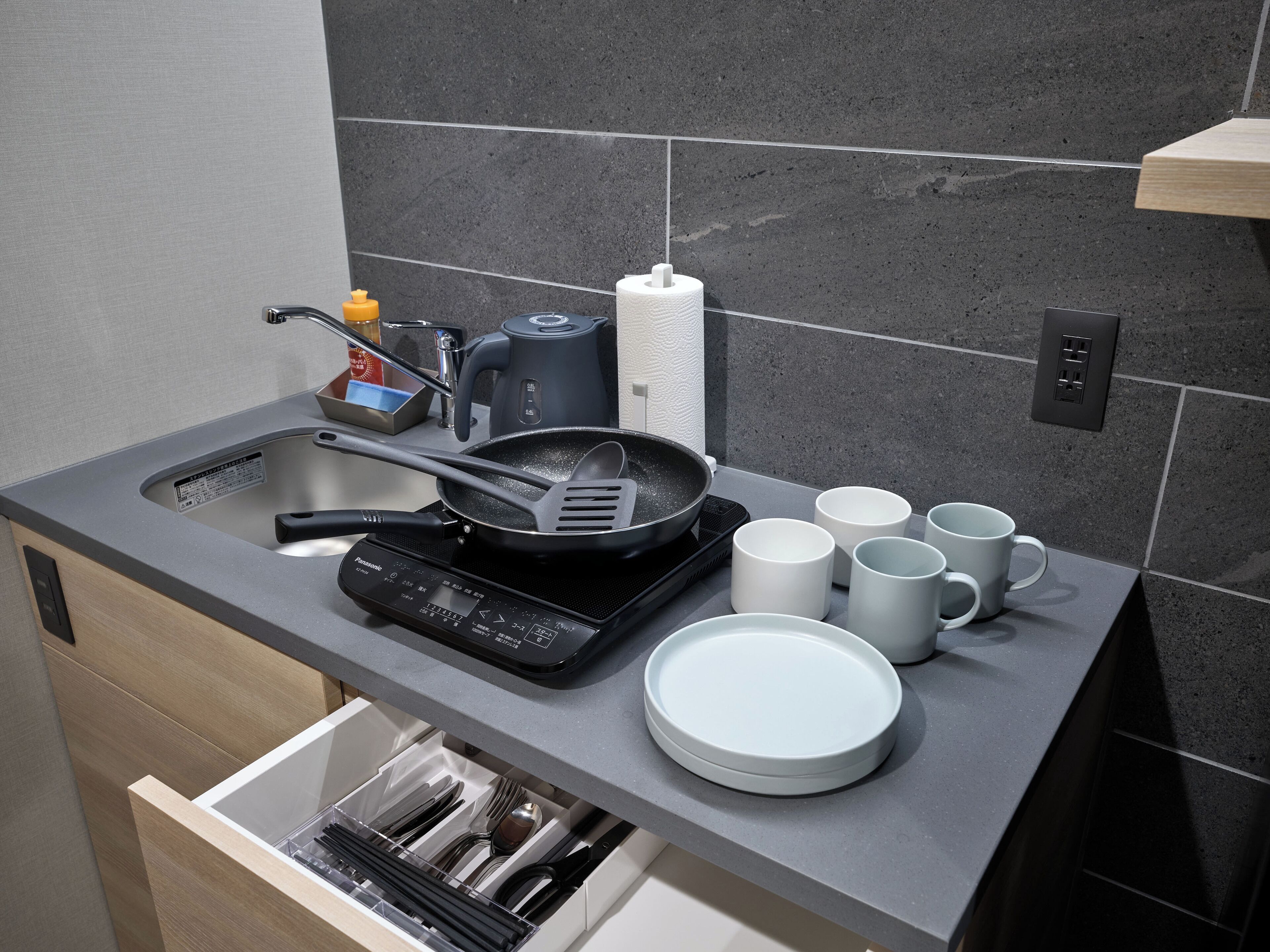 Una cocina moderna con lavavajillas integrado, cafetera, sartén y varias tazas blancas.