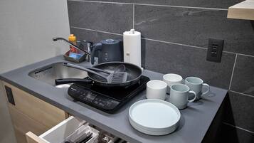 A modern kitchen with a built-in dishwasher, a coffee maker, a frying pan, and several white mugs.