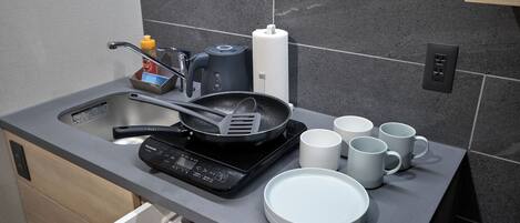 Una cocina moderna con lavavajillas integrado, cafetera, sartén y varias tazas blancas.